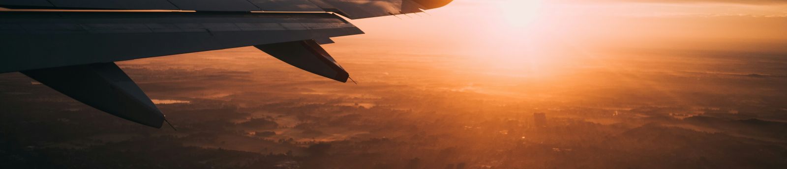 An airplane wing in the sky with the setting sun in the background