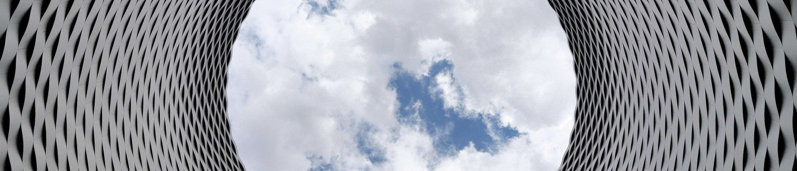 A column of mesh opening to clouds in a blue sky.